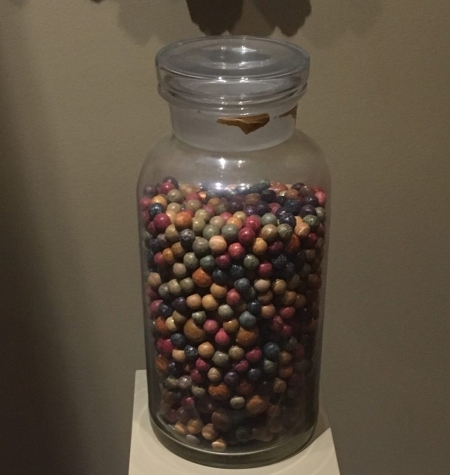A lidded glass jar almost full with many different colored marbles.