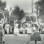 Three girls and a man dressed in traditional costumes carry flags and lead a parade for Fiesta Mexicana.