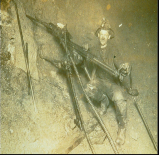 Photograph of a miner using a pneumatic rock drill in a mine.