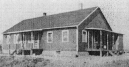 A very small image of a boarding house with two porches, one on the front and one on the side.