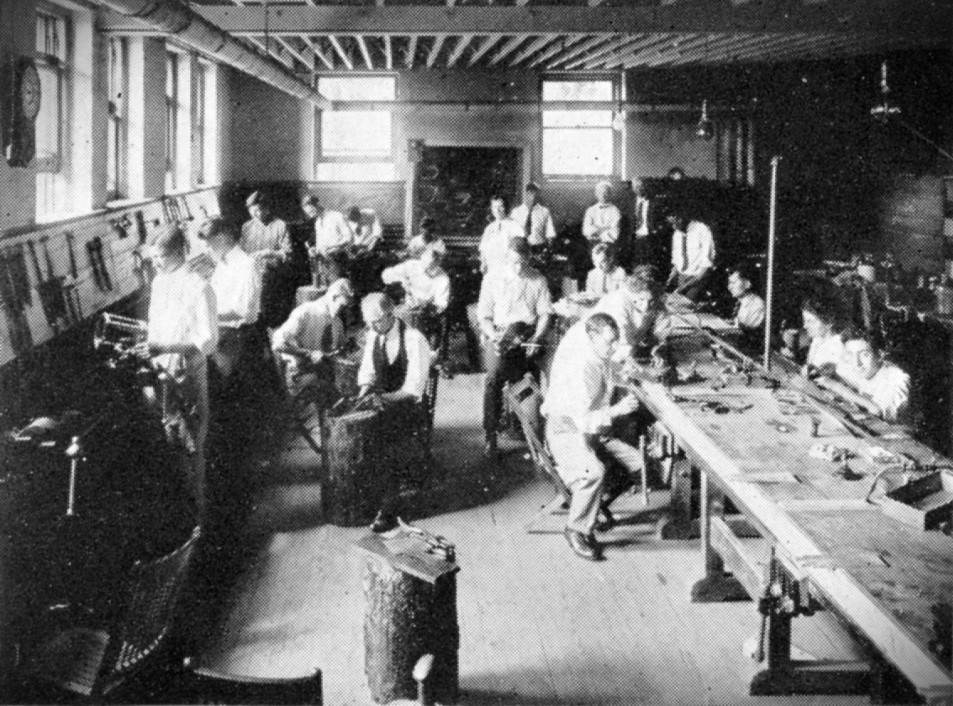 A photo of a metalworking classroom. Students are engaged in various metalworking activities along work tables.