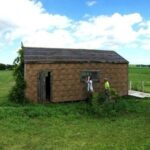A small wood frame building with small windows and asphalt siding.