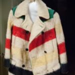 A picture of a white coat made out of a wool striped blanket, featuring red, yellow, green and black horizontal stripes.