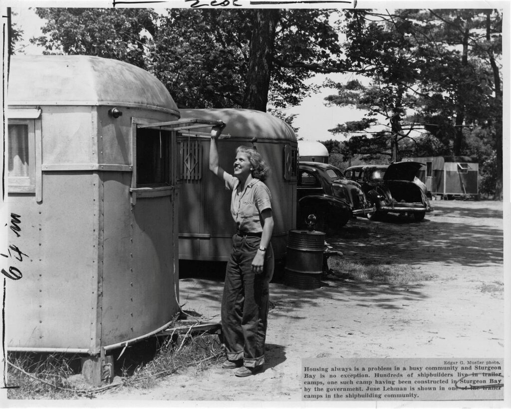 A woman poses next to a trailer home in a trailer camp.