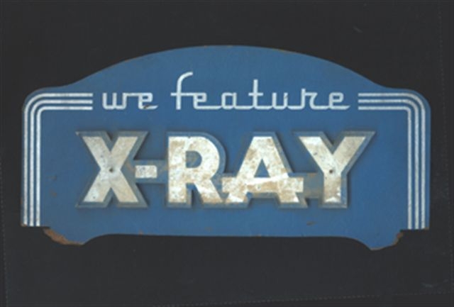 A steel and enamel sign that reads "We feature X-Ray." The sign is blue with white lettering.