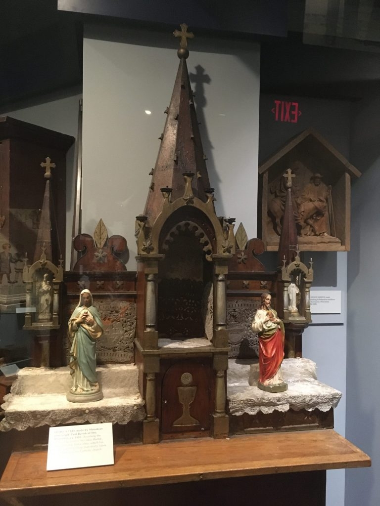 A wooden altar piece, with a tabernacle at the base, and Gothic Style ornamentation including three spires topped with Christian crosses.