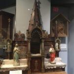 A wooden altar piece, with a tabernacle at the base, and Gothic Style ornamentation including three spires topped with Christian crosses.