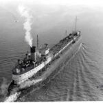 A black and white photo of a whaleback ship converted to be an oil tanker steaming across a lake