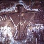 A thunderbird petroglyph carved into a sandstone wall, outlined in white chalk.