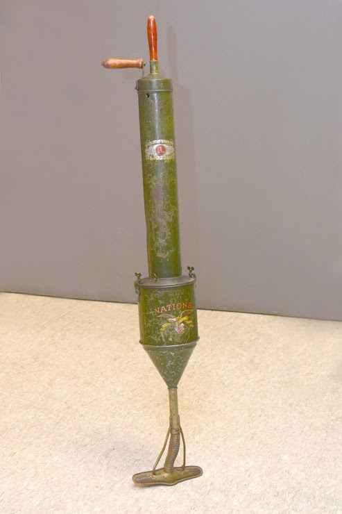A hand-pump vacuum cleaner, green metal with glass cleaner head and wooden handles