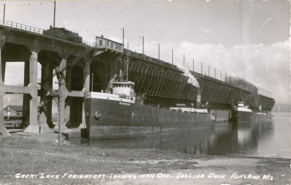 Historic photograph from shoreline towards three ore boats at the Soo Line Railroad dock being loaded with iron ore.