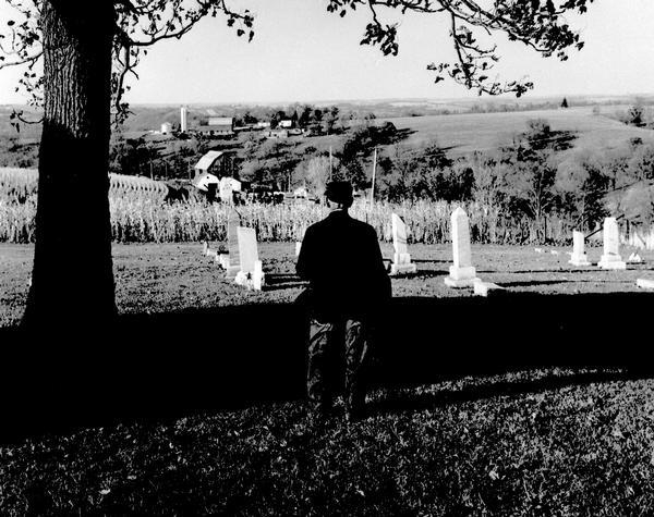 A man, with his back to the camera, looks out over a graveyard.