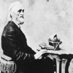 Portrait of Christopher Latham Sholes posing at a typewriter.