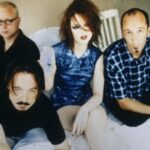 Color publicity photograph of the band members from Garbage, a Madison, Wisconsin rock band. They are sitting or leaning on a bed with white linens.