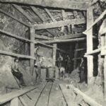 View inside a lead mine showing six miners with a car on a track.