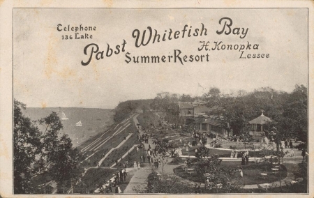A black-and-white photographic postcard with the title, “Pabst Whitefish Bay Summer Resort.” The image shows an aerial view of the resort grounds overlooking Lake Michigan.