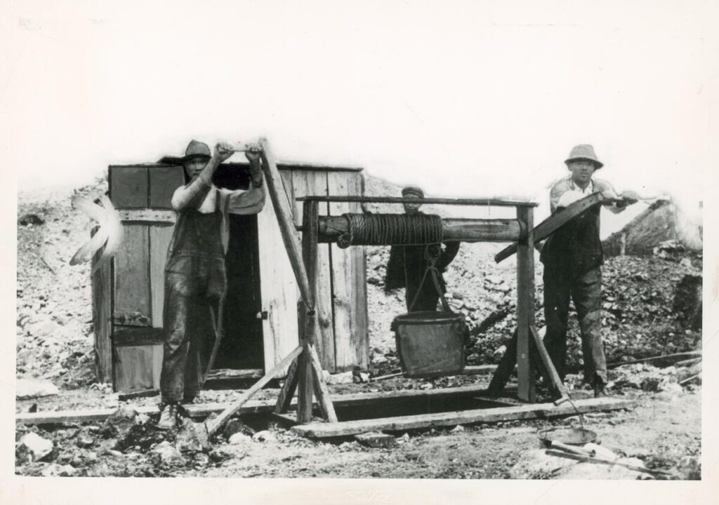 Three miners pose with a windlass.