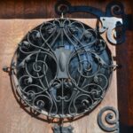 Detail of the round window of the Wilson Place Mansion door, featuring an intricate wrought iron screen of intertwining vines and acanthus leaves around a central cartouche.