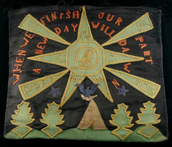 A black pillowcase with embroidery and applique, featuring a CCC emblem, an eagle over a tent, applique trees, and embroidered text, “When we finish our part a new day will dawn.”