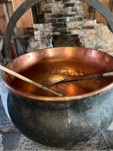 Copper cheese kettle, blackened on the exterior, cauldron-like with steel handle.