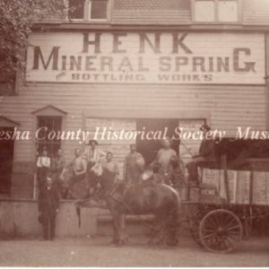 Henk Mineral Spring employees pictured outside the bottling plant with a loaded horse-drawn wagon. Owner August Henk stands to the left of the horse, and one employee holds a bottle of water. 1918. Image courtesy of Waukesha County Historical Society & Museum Collection ID: 2006.715.