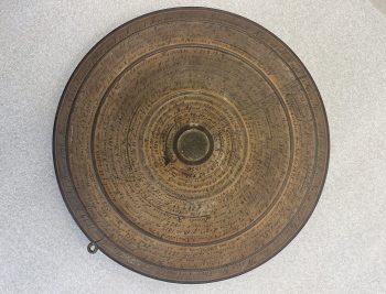 A wooden disk with a coin embedded at the center and writing in concentric circles covering the surface.