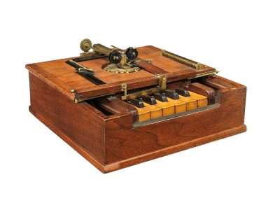 An early typing machine. It looks something like a small wooden box with a piano keyboard with only 11 keys.