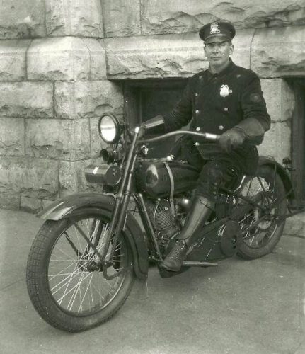 Black and white photograph of a policeman posed on a motorcycle.