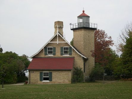 Photograph of a lighthouse. The lighthouse and keepers station are both built of brick. The lighthouse is just taller than the house, and is square with a round lantern.