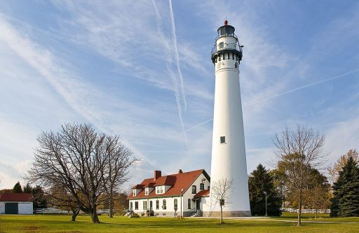 Photograph of the Wind Point Lighthouse and keepers house. The lighthouse towers over the house. The tower, constructed of brick, stuccoed, and painted white, is round and has an observation deck that encircles the lantern.