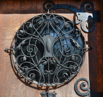 Detail of the round window of the Wilson Place Mansion door, featuring an intricate wrought iron screen of intertwining vines and acanthus leaves around a central cartouche.