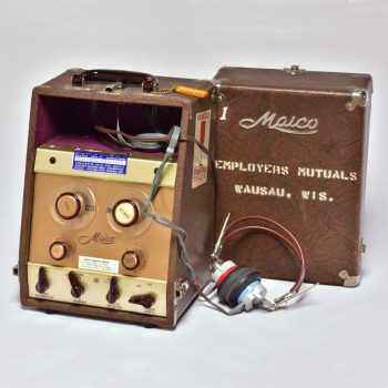 Color photograph of a audiometer, which looks a bit like a box with knobs and wires coming out of it.